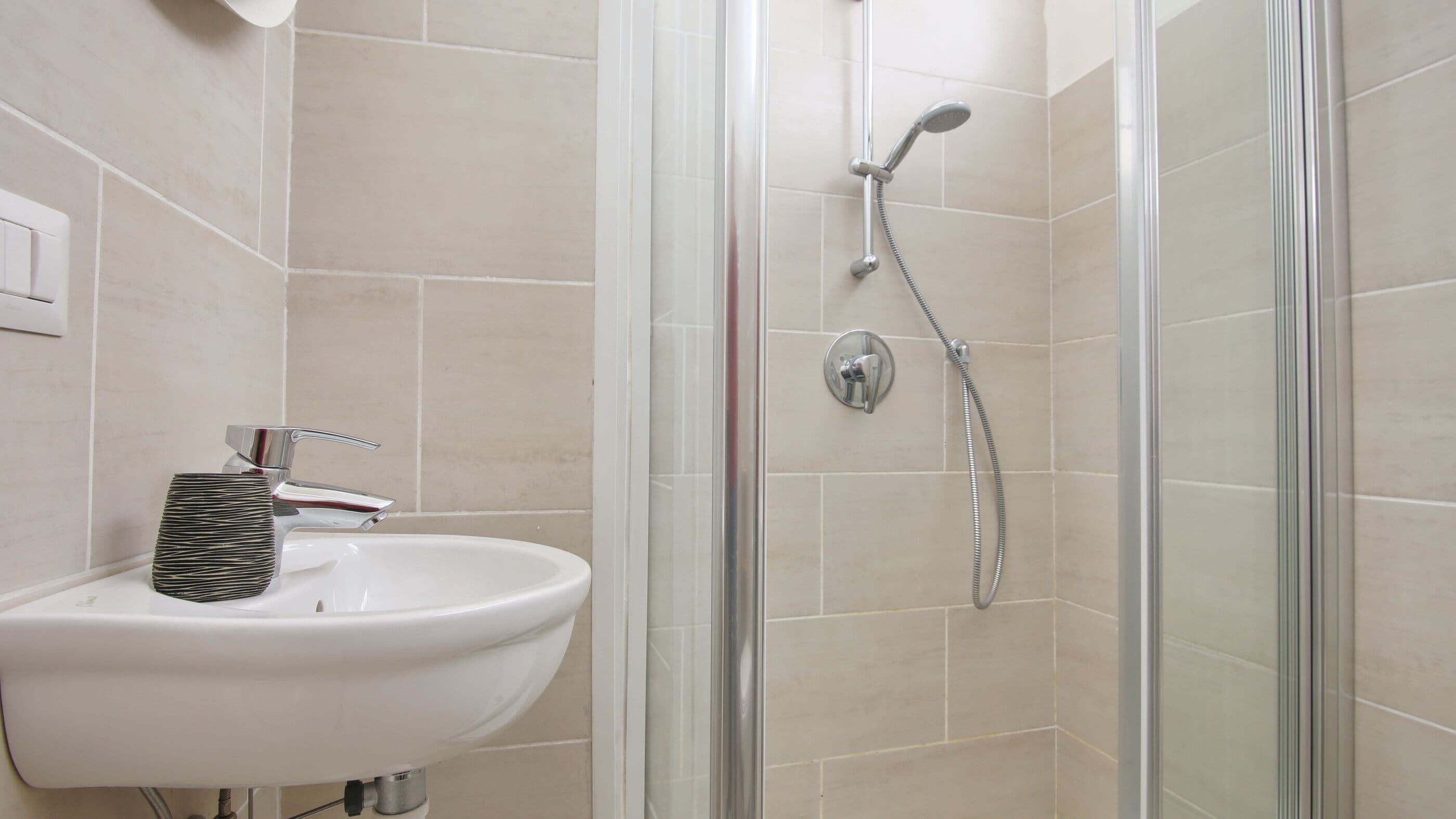 A bathroom with a white sink, a glass shower enclosure, and beige tiles.