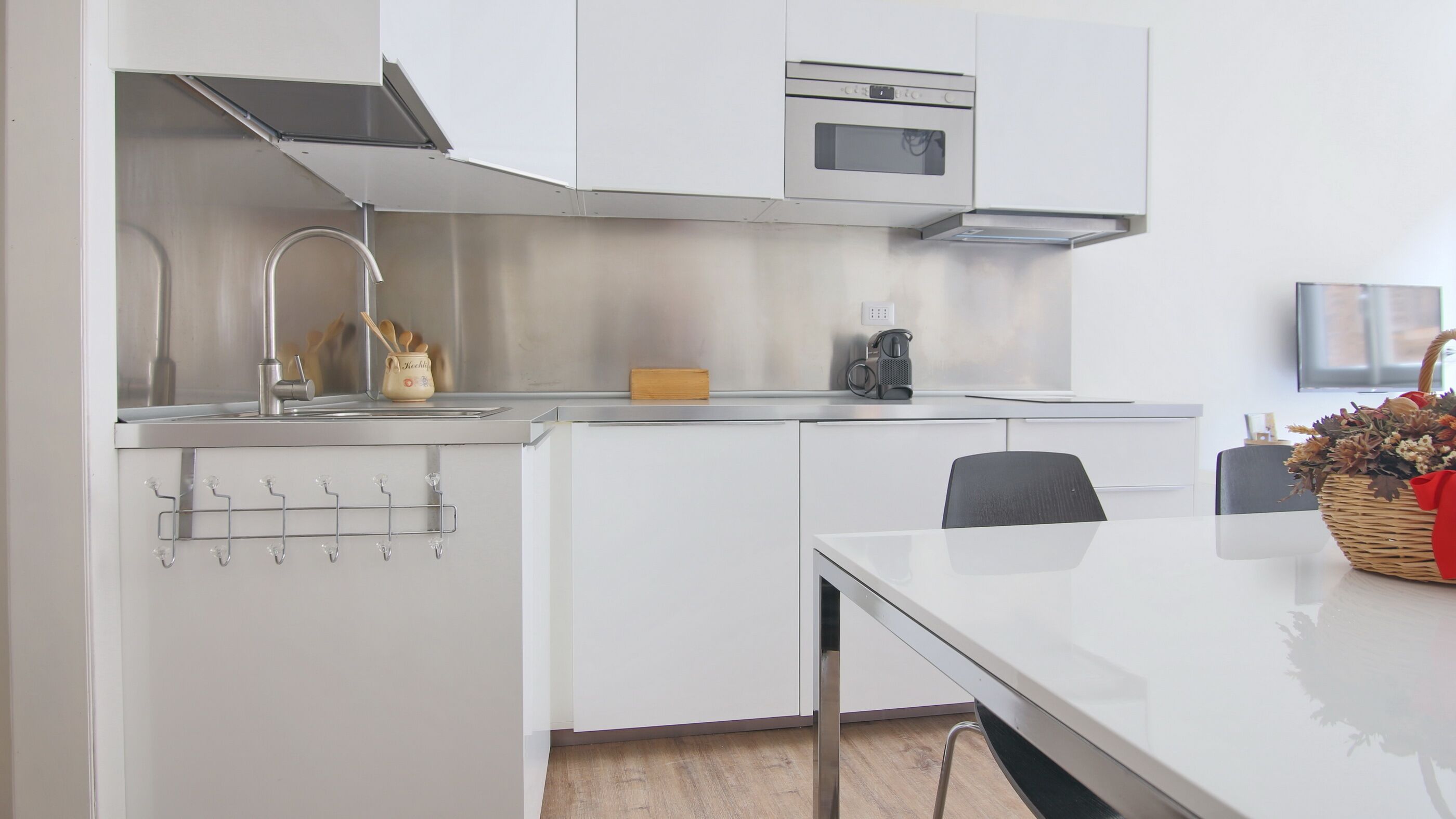 A modern kitchen with white cabinetry, a stainless steel range hood, a microwave, and a coffee maker.