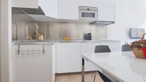 Eine moderne Küche mit weißen Schränken, einer Edelstahl-Dunstabzugshaube, einer Mikrowelle und einer Kaffeemaschine.