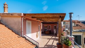 A rooftop terrace with a wooden pergola, a door, and a small table with chairs.