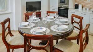 Zona pranzo con un tavolo rotondo in vetro apparecchiato per quattro persone, circondato da sedie di legno con sedili imbottiti.