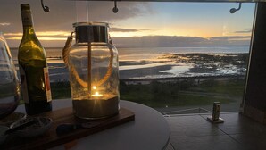 A table with a bottle and a candle holder, overlooking a scenic view of a body of water and distant mountains.