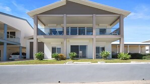A modern two-story building with a flat roof, large glass windows, and a balcony on the upper floor.