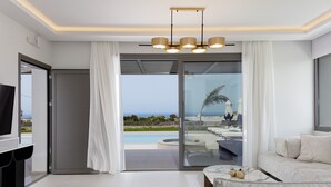 Una sala moderna con un sofá, una mesa de centro y un televisor. Cuenta con un ventanal corredizo que da a una zona de piscina con vista al océano.