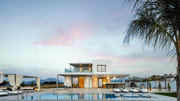 Una casa moderna de dos pisos con piscina, mobiliario exterior y vistas a las montañas.