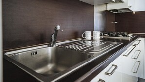 Una cocina moderna con un lavamanos de acero inoxidable, un grifo y una estufa. Hay dos tazas blancas sobre la encimera.