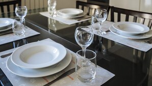 Una mesa de comedor con platos blancos, vasos transparentes y cubiertos sobre caminos de mesa con iconos.