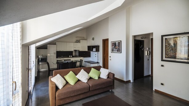 Una sala de estar moderna con un sofá marrón, una mesa de comedor y una cocina al fondo.
