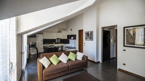 A modern living room with a brown sofa, a dining table, and a kitchen in the background.