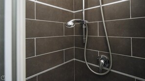 A shower area with a handheld showerhead and a wall-mounted faucet.
