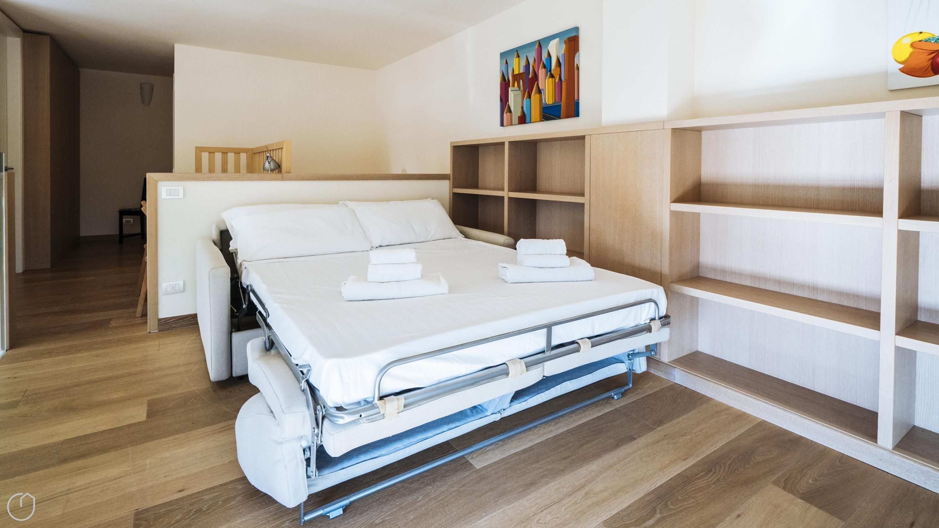 Ein kompakter Raum mit einem Klappbett, einer hölzernen Bank, einem kleinen Tisch und einem an der Wand befestigten Regal.