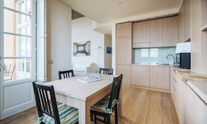 A compact kitchen with wooden cabinets, a dining table with chairs, and a view through an open window.