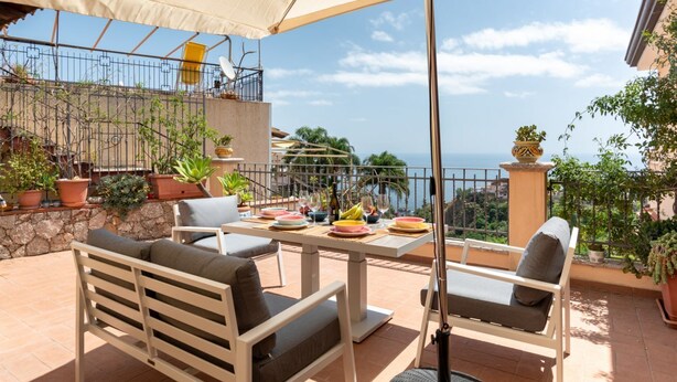 Une terrasse extérieure avec une table dressée pour le repas, des chaises et un grand parasol.