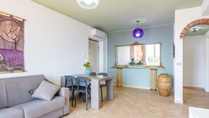 Un salon comprenant un canapé, une table à manger avec des chaises, un grand miroir et un luminaire suspendu.