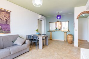 Un salon comprenant un canapé, une table à manger avec des chaises, un grand miroir et un luminaire suspendu.