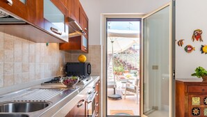 Une cuisine équipée d’un évier à deux bacs, d’une cuisinière et d’un four à micro-ondes. Une porte-fenêtre coulissante donne accès à un patio extérieur.