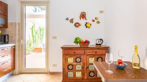 Une cuisine avec des meubles en bois, une table à manger sur laquelle se trouve un saladier rempli de fruits et une bouteille de vin, et un mur orné de masques de poissons décoratifs.