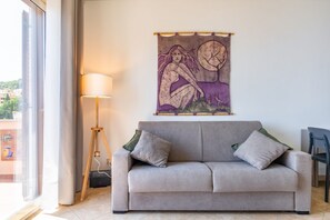 En stue med sofa, lampe og et gobelin på væggen.