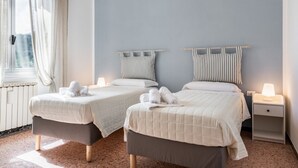 A hotel room with two beds, a window with curtains, a bedside lamp, and a ceiling light fixture.