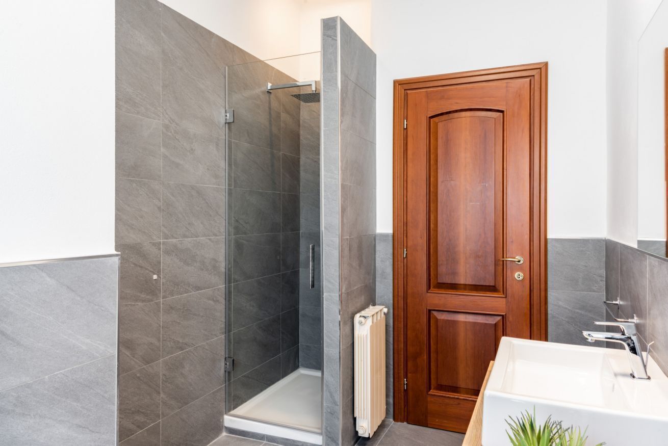 A bathroom with a shower, a wooden door, and a white sink.