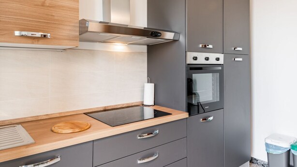 A modern kitchen with grey cabinets, a stainless steel range hood, a built-in oven, and a wooden countertop.