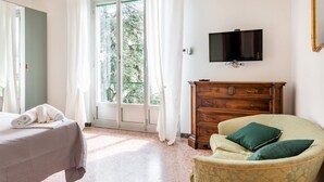 A hotel room with a bed, a chair, a dresser, a television, and a sliding glass door to the outside.
