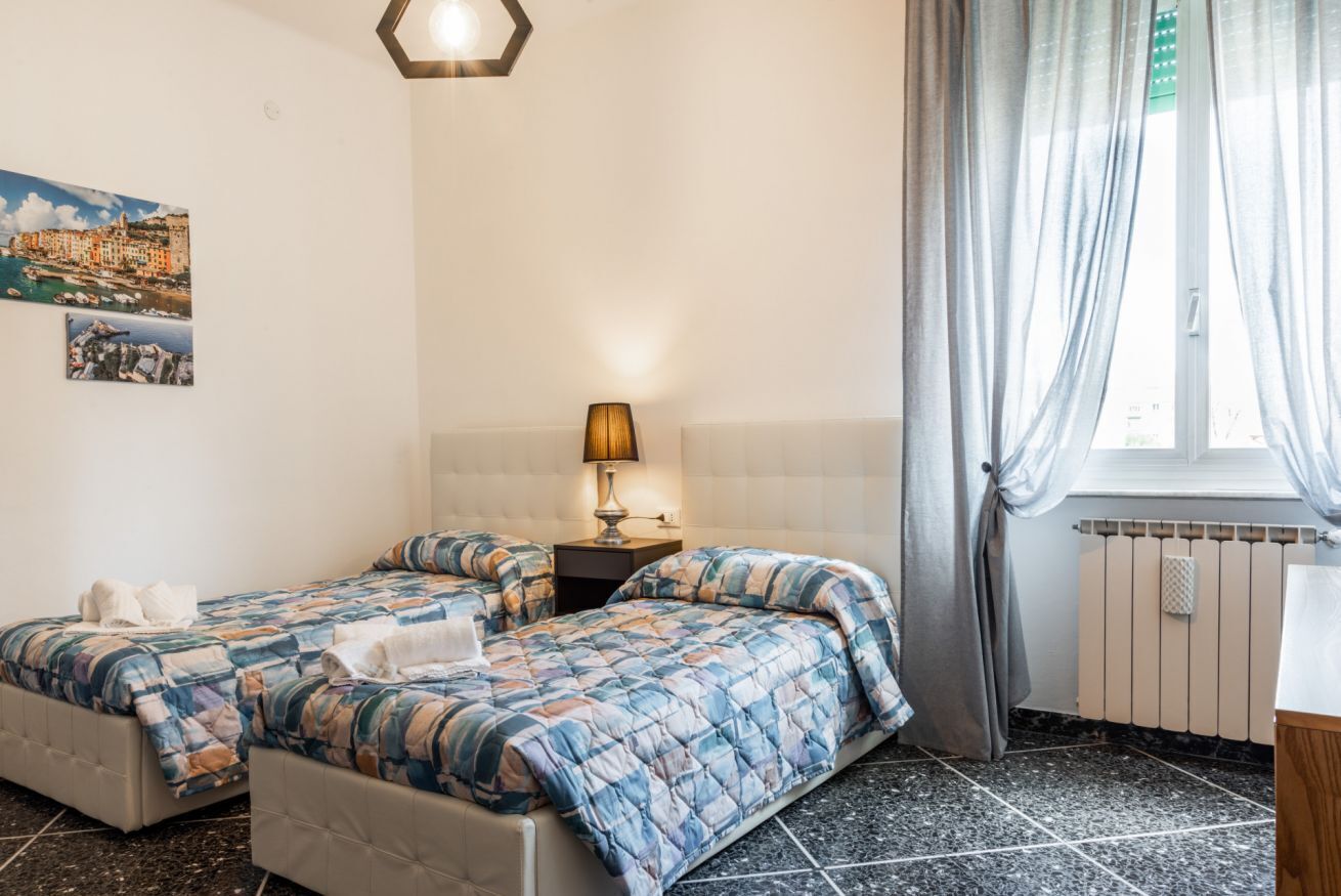 Une chambre d’hôtel avec deux lits, une table de chevet avec une lampe, une fenêtre avec des rideaux et un radiateur.