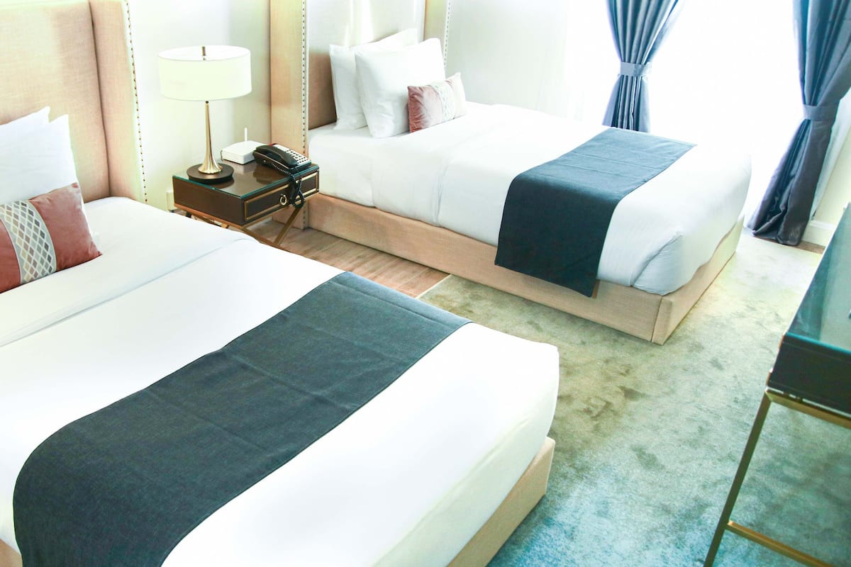 A hotel room with two beds, a bedside table with a lamp, a telephone, and a mirror.