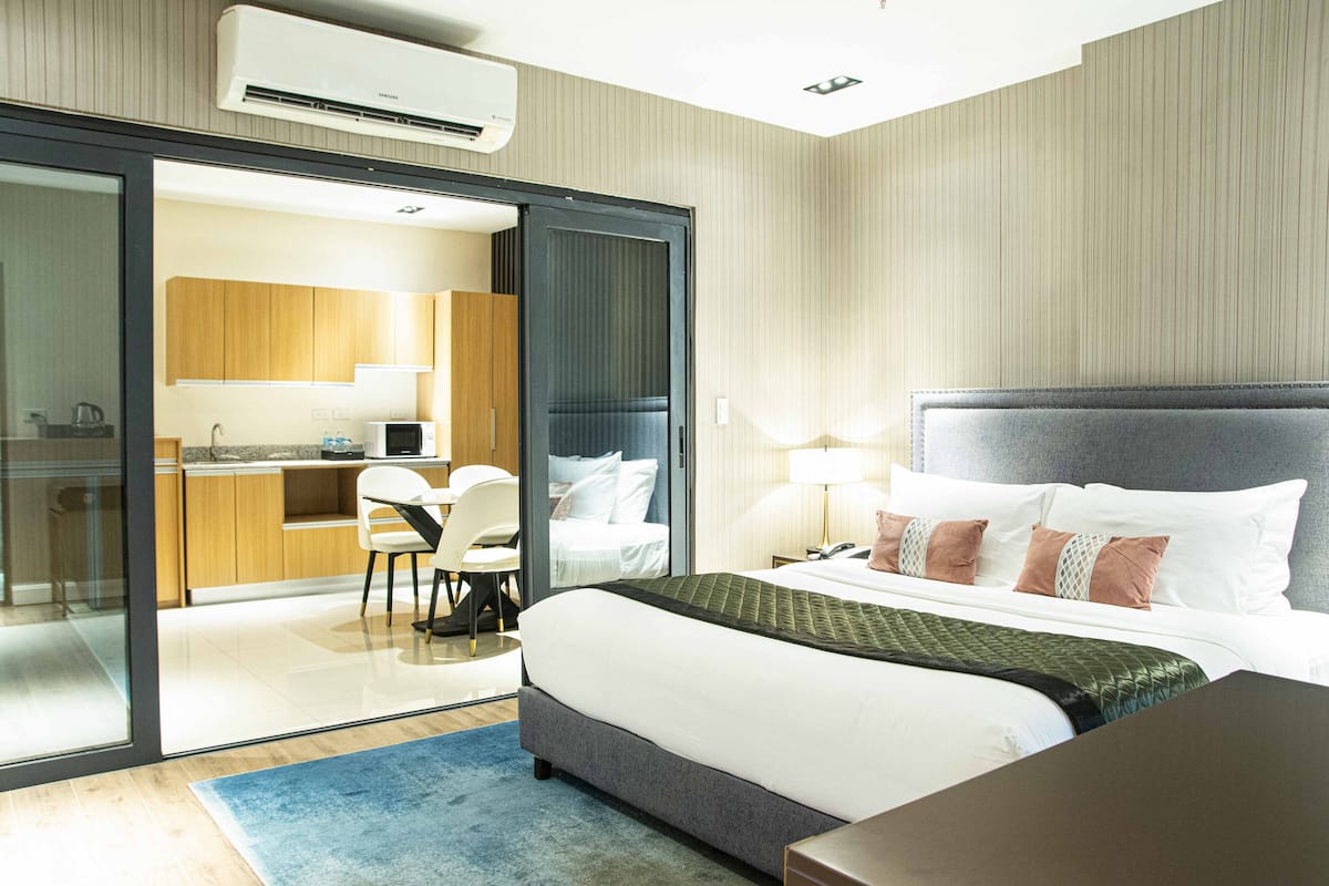 A modern hotel room with a large bed, a desk, and a kitchenette.