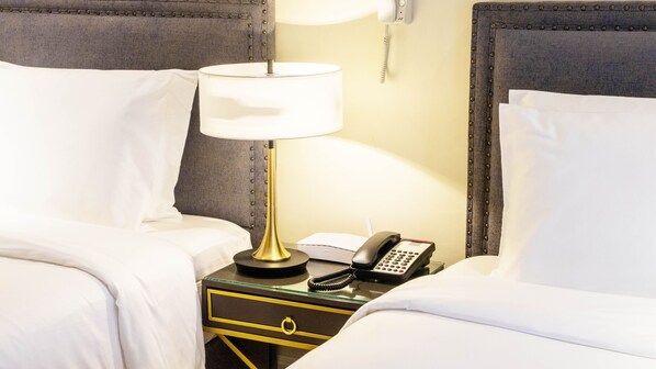 A hotel room with a bed, a bedside lamp, a telephone, and a small drawer with a ring handle.
