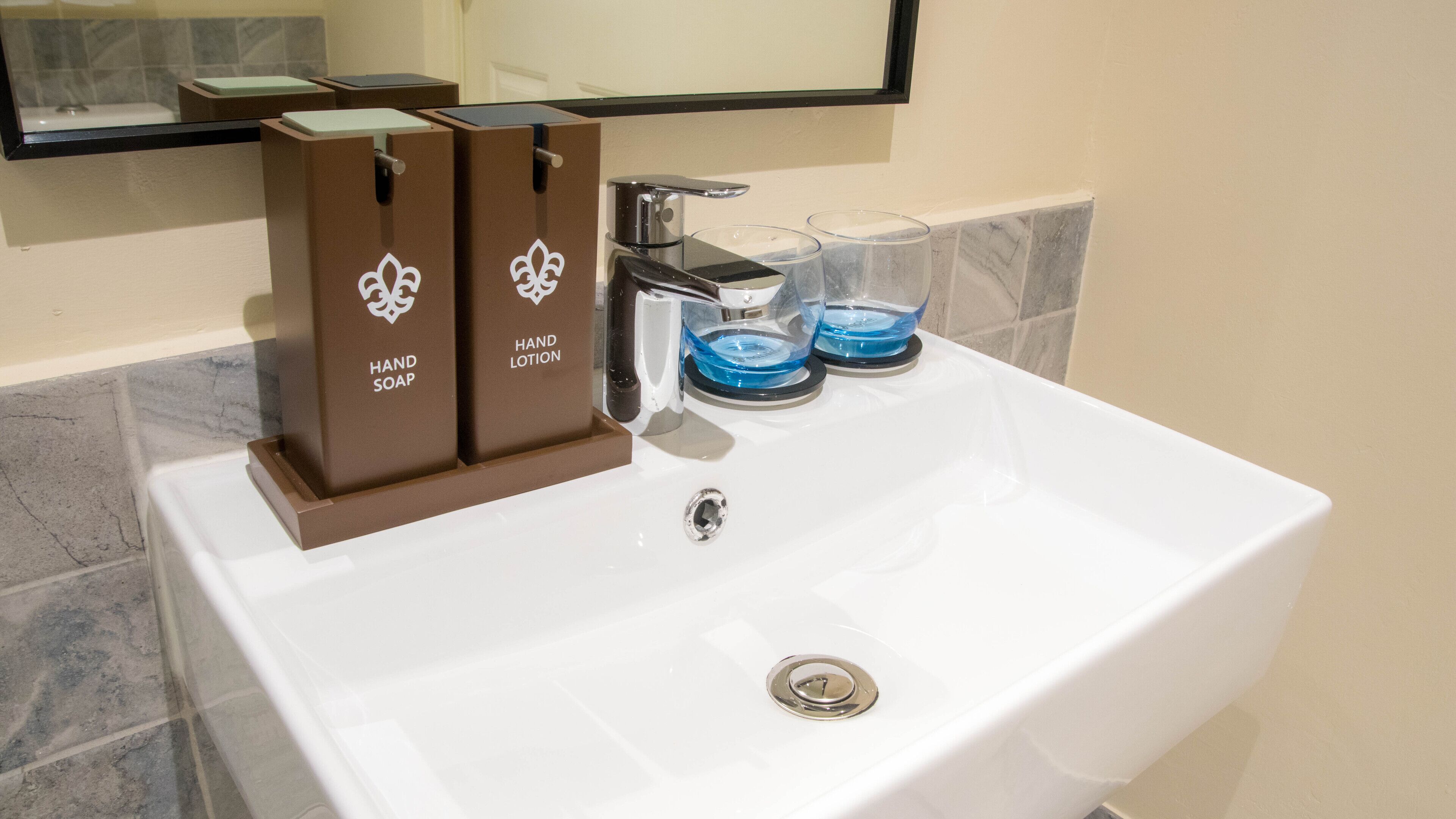 A white bathroom sink with two brown dispensers labeled "HAND SOAP" and "HAND LOTION".