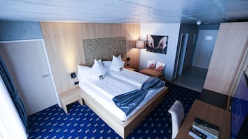 A hotel room with a bed, bedside table, lamp, and a small desk with a chair.