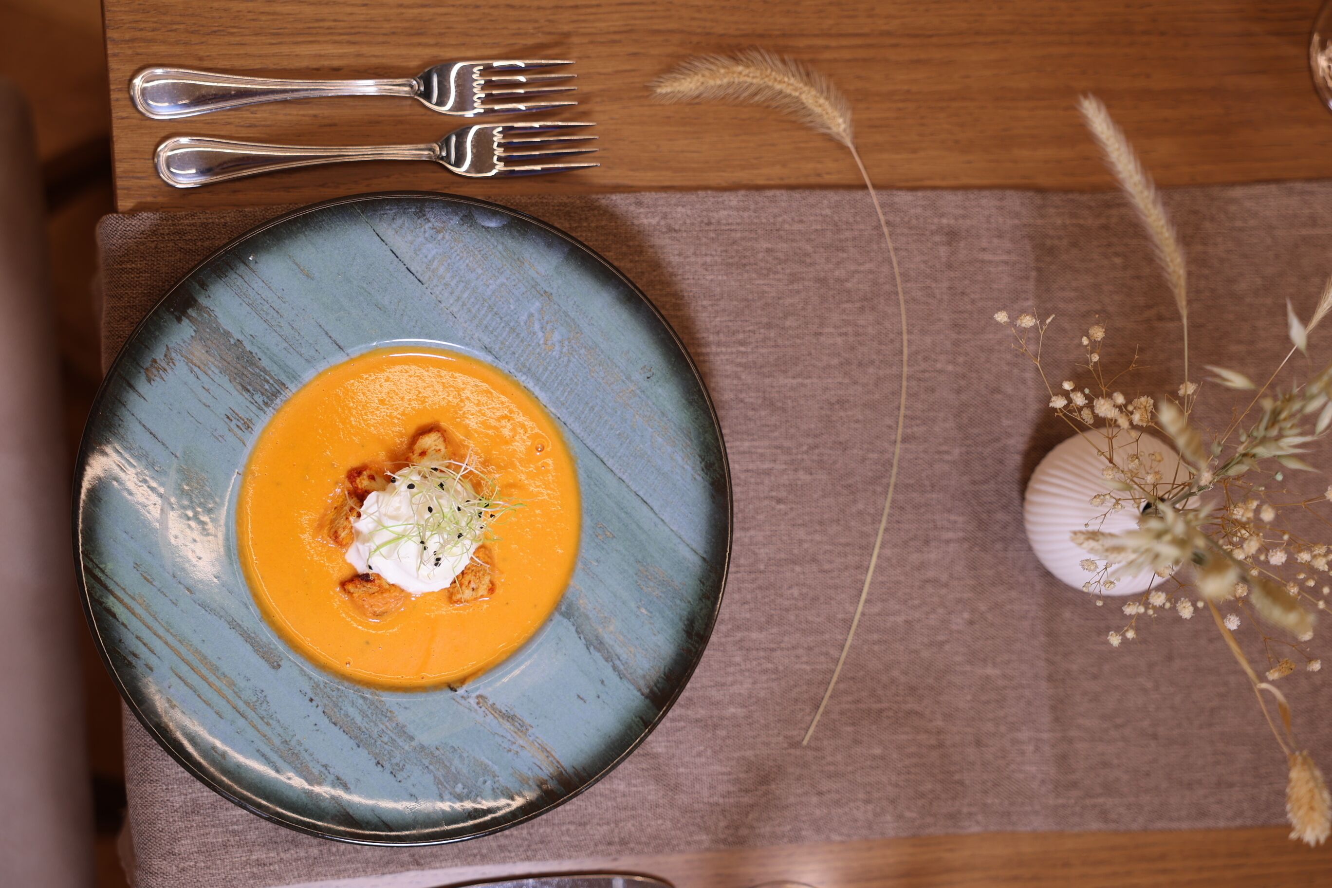 Un plato de sopa con guarnición, acompañado de un tenedor y una cuchara sobre una mesa de madera.