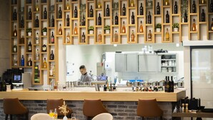 Una zona de bar con mostrador de madera, diversas opciones de asientos y una pared repleta de botellas de vino.