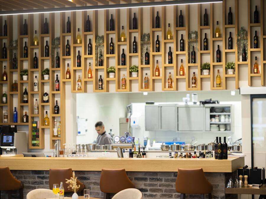 Una zona de bar con mostrador de madera, diversas opciones de asientos y una pared repleta de botellas de vino.
