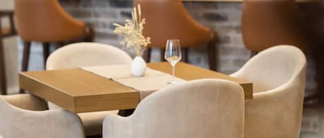A restaurant interior with a bar area, wooden chairs, and a table with a vase and glass.