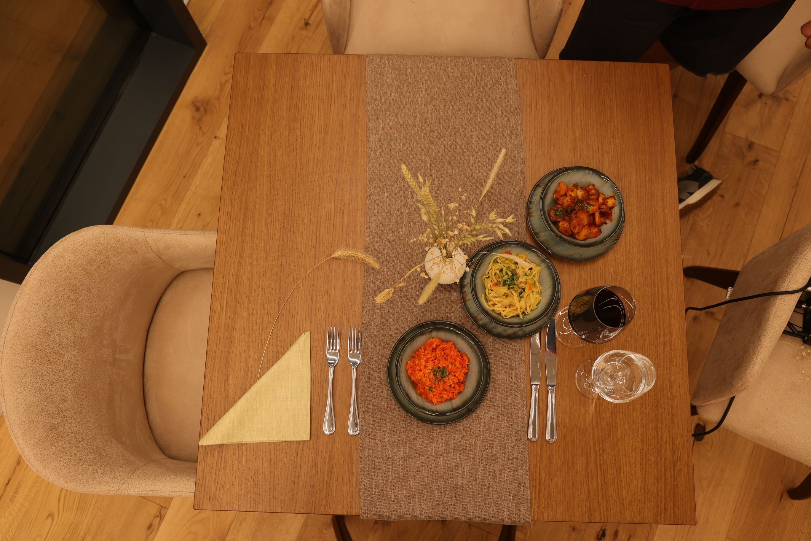 Une table à manger avec trois assiettes de nourriture, un vase contenant des fleurs séchées et des couverts.