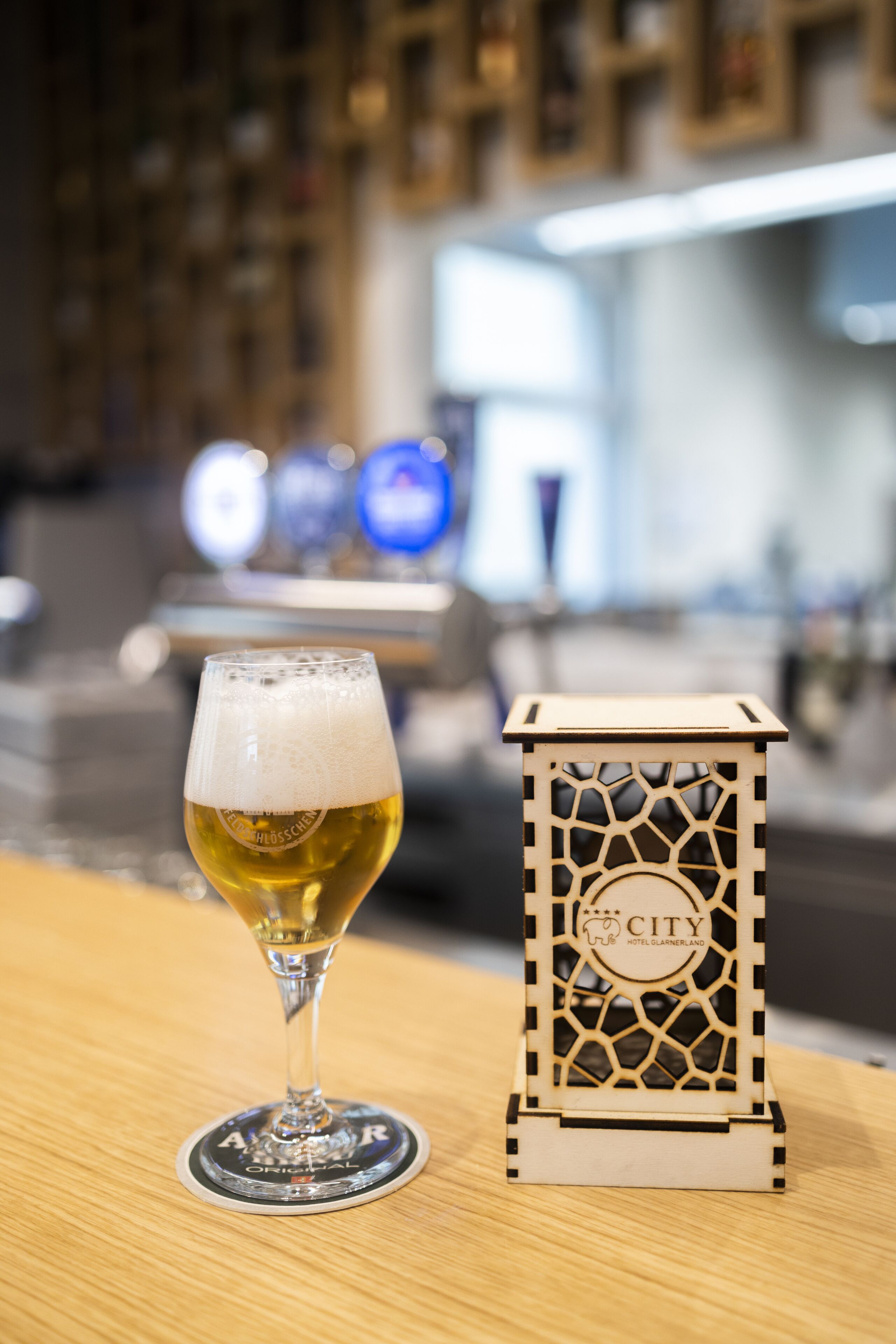 Una cerveza en un posavasos, con un cartel de madera al fondo.