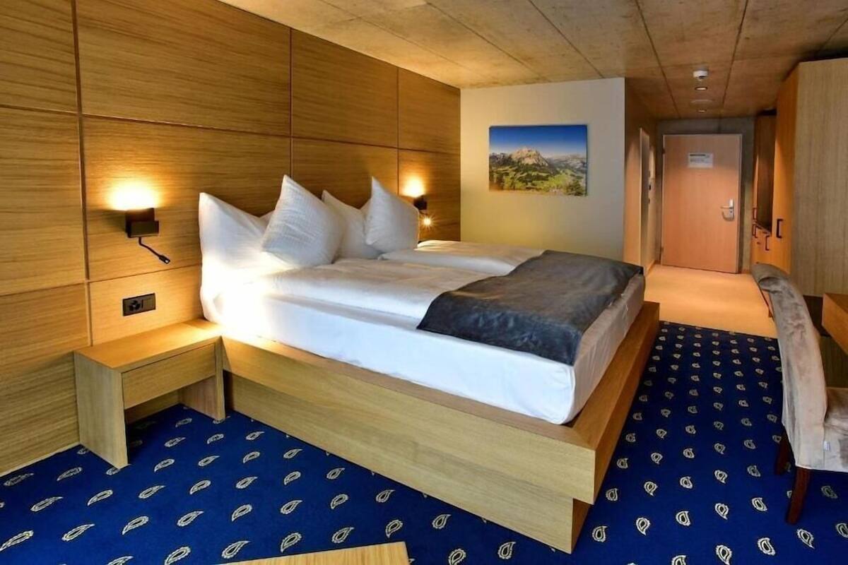 Una habitación con una cama, mesitas de noche, una lámpara de pared y una puerta.