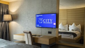 Habitación de hotel con cama, escritorio y televisor mostrando el nombre del hotel y sus servicios.