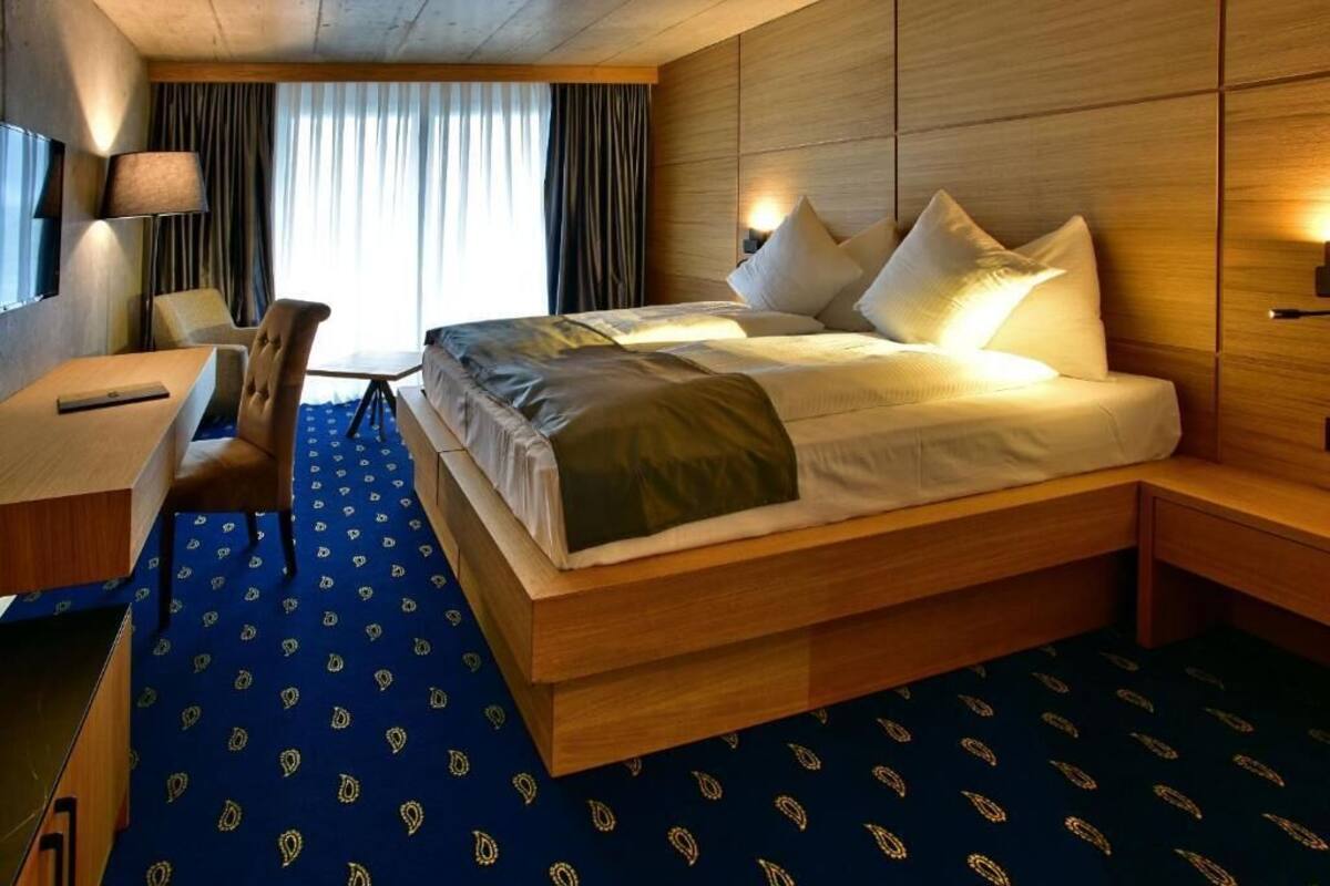 Una habitación de hotel con una cama grande, mesitas de noche, un escritorio y una silla.