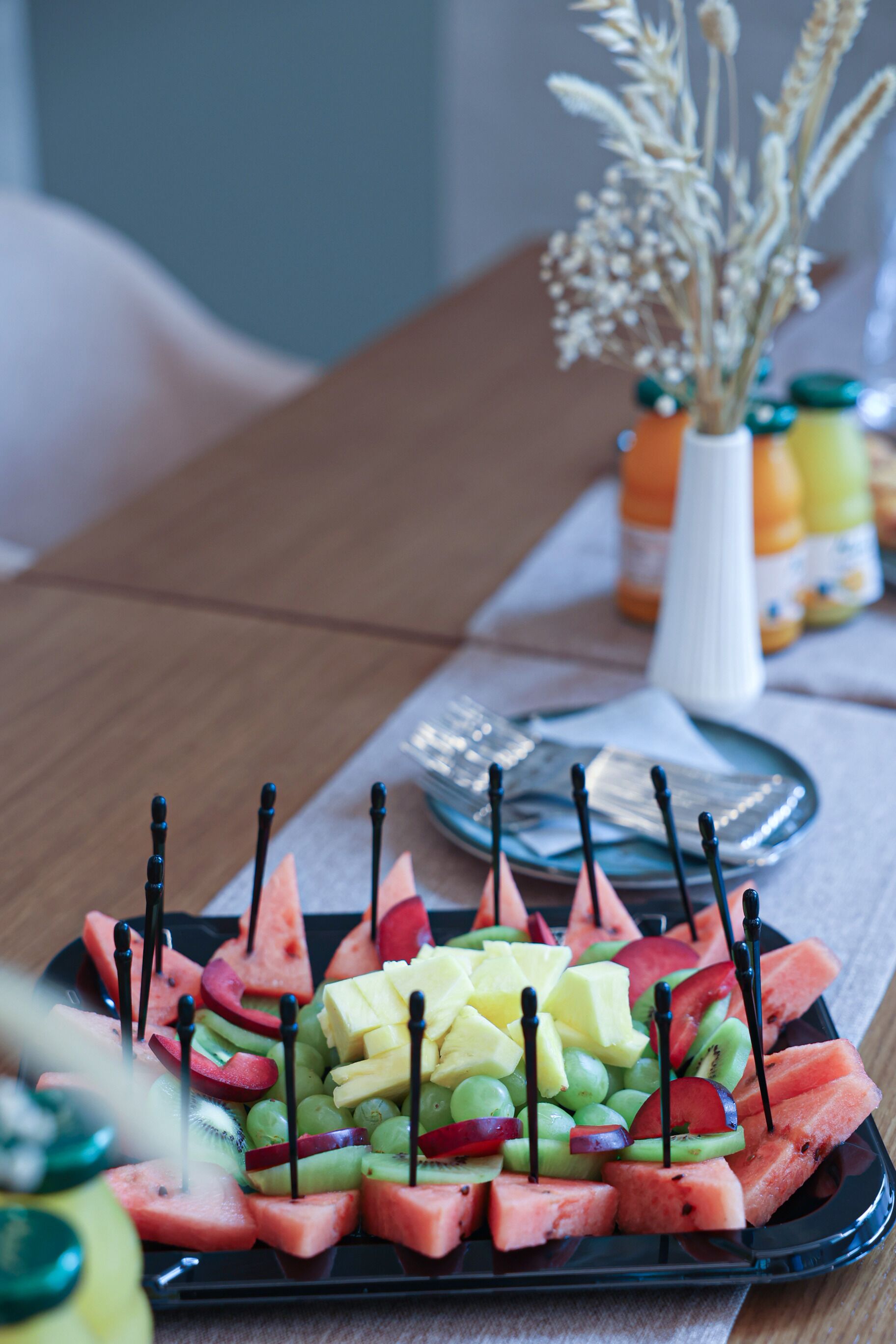 Una bandeja negra con una fuente de frutas variadas y palillos de dientes.