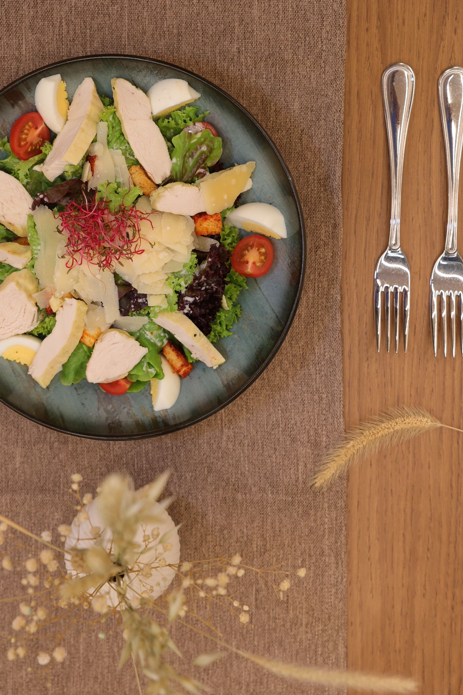 Ensalada con varios ingredientes, acompañada de dos tenedores sobre una mesa de madera.