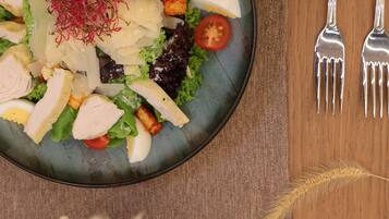 A plate of salad with various ingredients, accompanied by two forks on a wooden table.