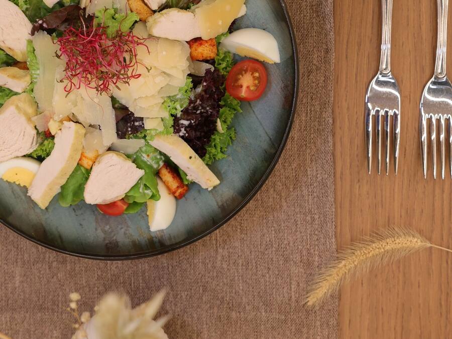 A plate of salad with various ingredients, accompanied by two forks on a wooden table.