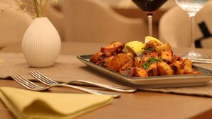 Una mesa de comedor con un plato de comida, dos copas de vino y un florero con espigas de trigo.