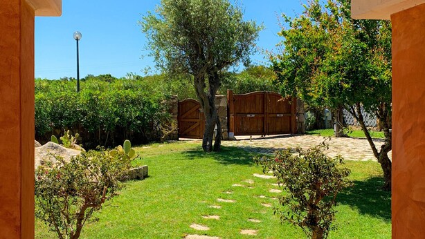 An outdoor pathway leading to a building with a stone wall and a wooden gate.