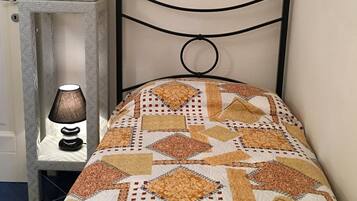 A bed with a patterned quilt, a bedside table with a lamp, and a wall-mounted headboard.