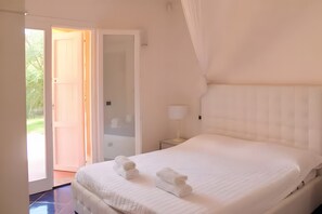 A bedroom with a bed, a nightstand, a lamp, and an open door leading to a balcony.