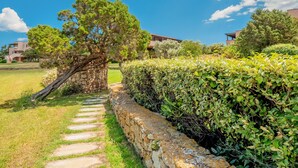 A stone pathway leading to a building with a large tree and a hedge. - "Casa Vacanze Miky Punta Asfodeli" Apartment with Terrace, Garden & A/C (Portorotondo)